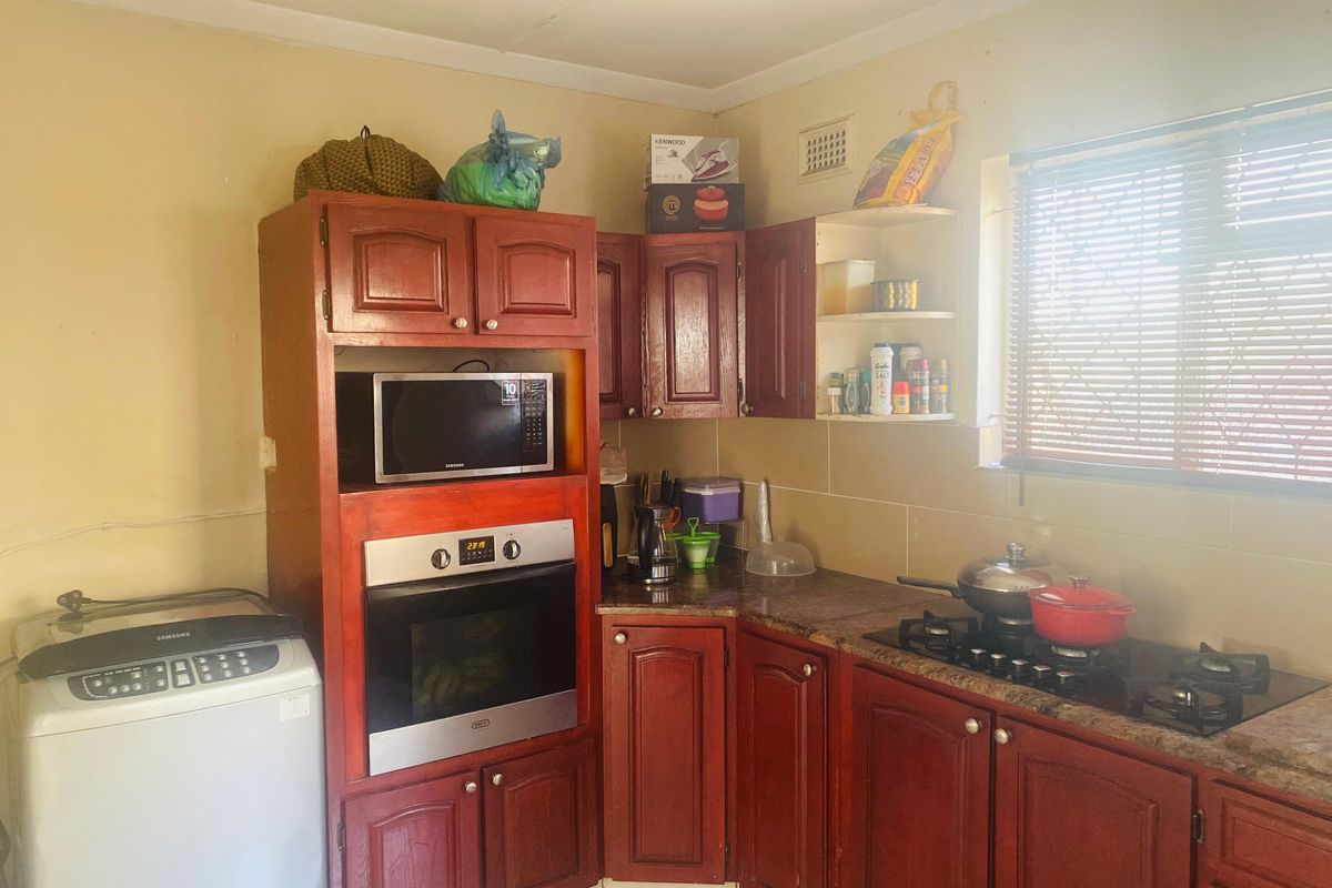 A functional kitchen featuring dark wood cabinetry, granite countertops, a built-in oven, and a gas hob, with space for a washing machine.