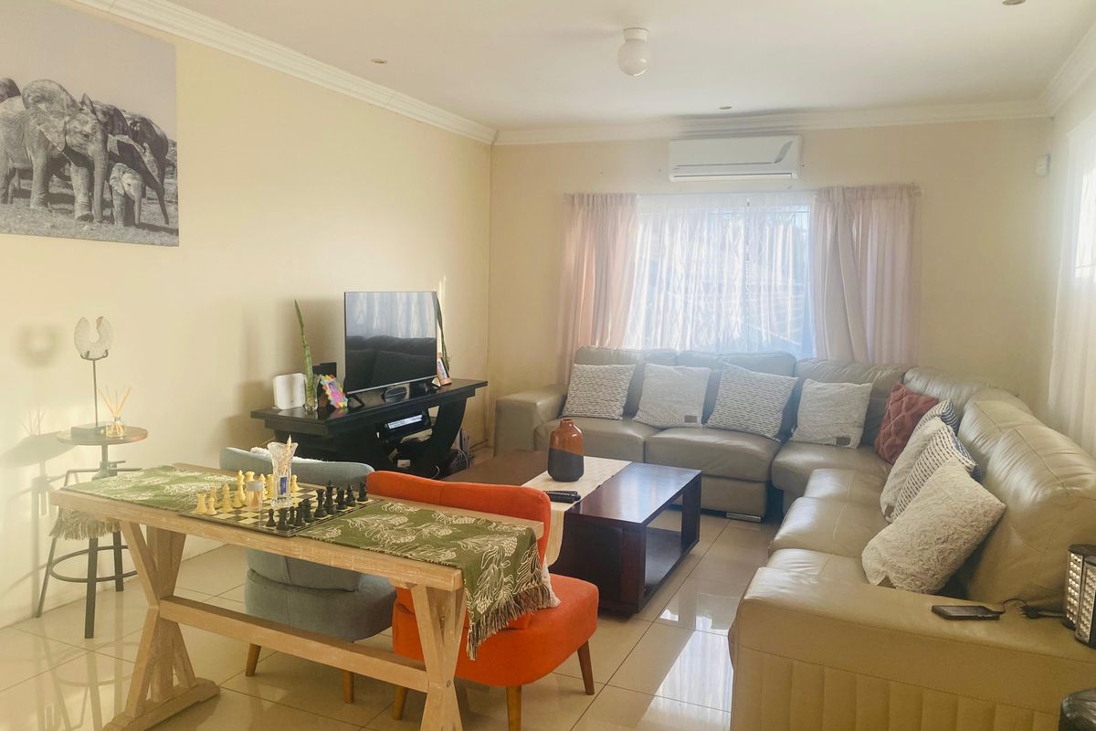 A comfortable living room featuring tiled flooring, recessed downlighting, and a wall-mounted split-system air conditioner for climate control.