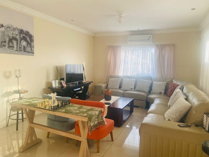 A comfortable living room featuring tiled flooring, recessed downlighting, and a wall-mounted split-system air conditioner for climate control.