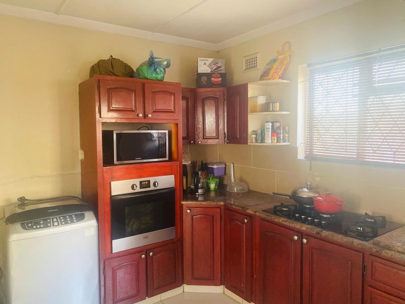 A functional kitchen featuring dark wood cabinetry, granite countertops, a built-in oven, and a gas hob, with a window providing natural light.