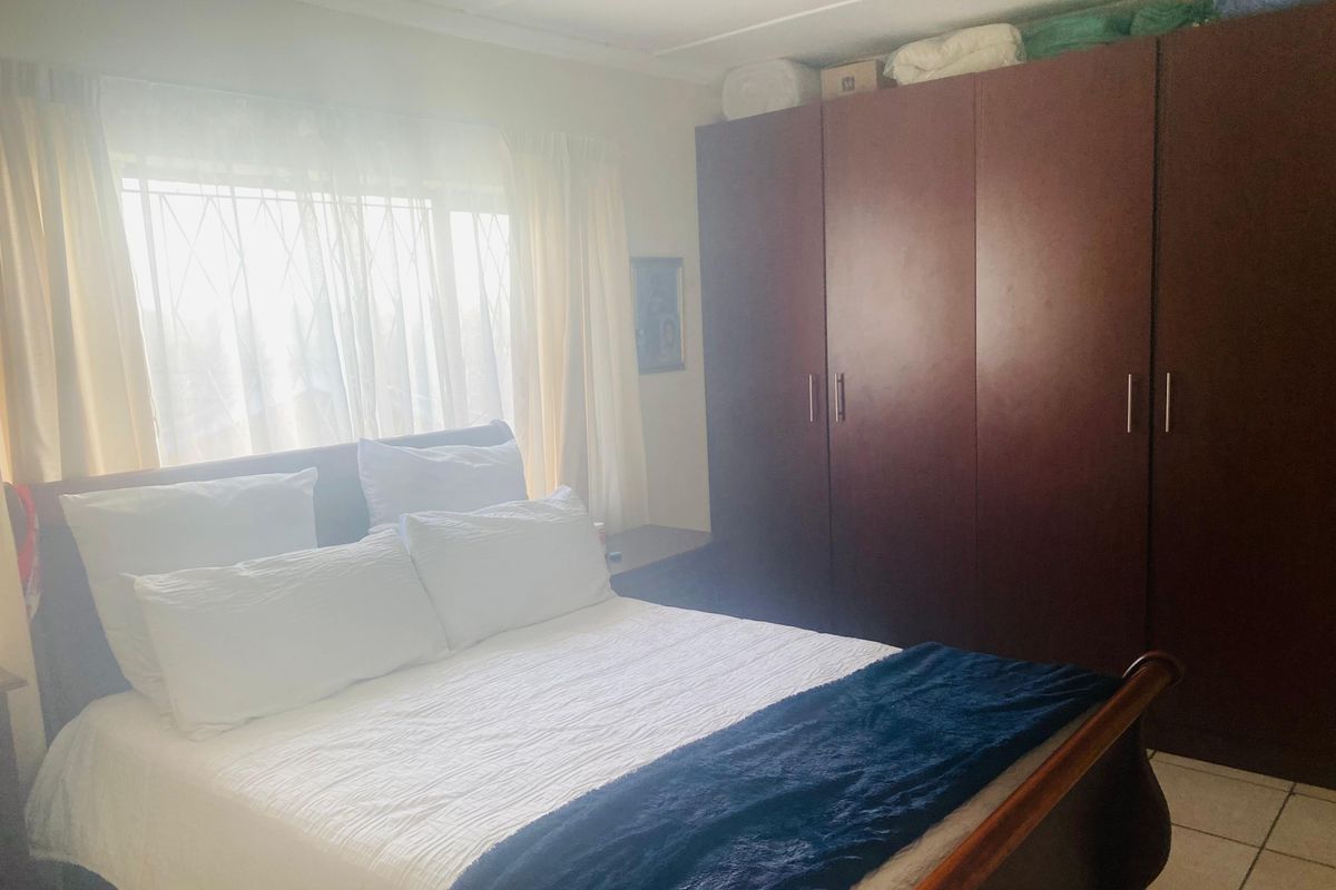 A bedroom featuring a large built-in wardrobe and security bars on the window, providing a functional and secure living space.