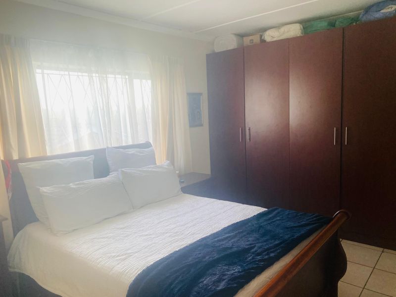 A bedroom featuring a large built-in wardrobe and security bars on the window, providing a functional and secure living space.