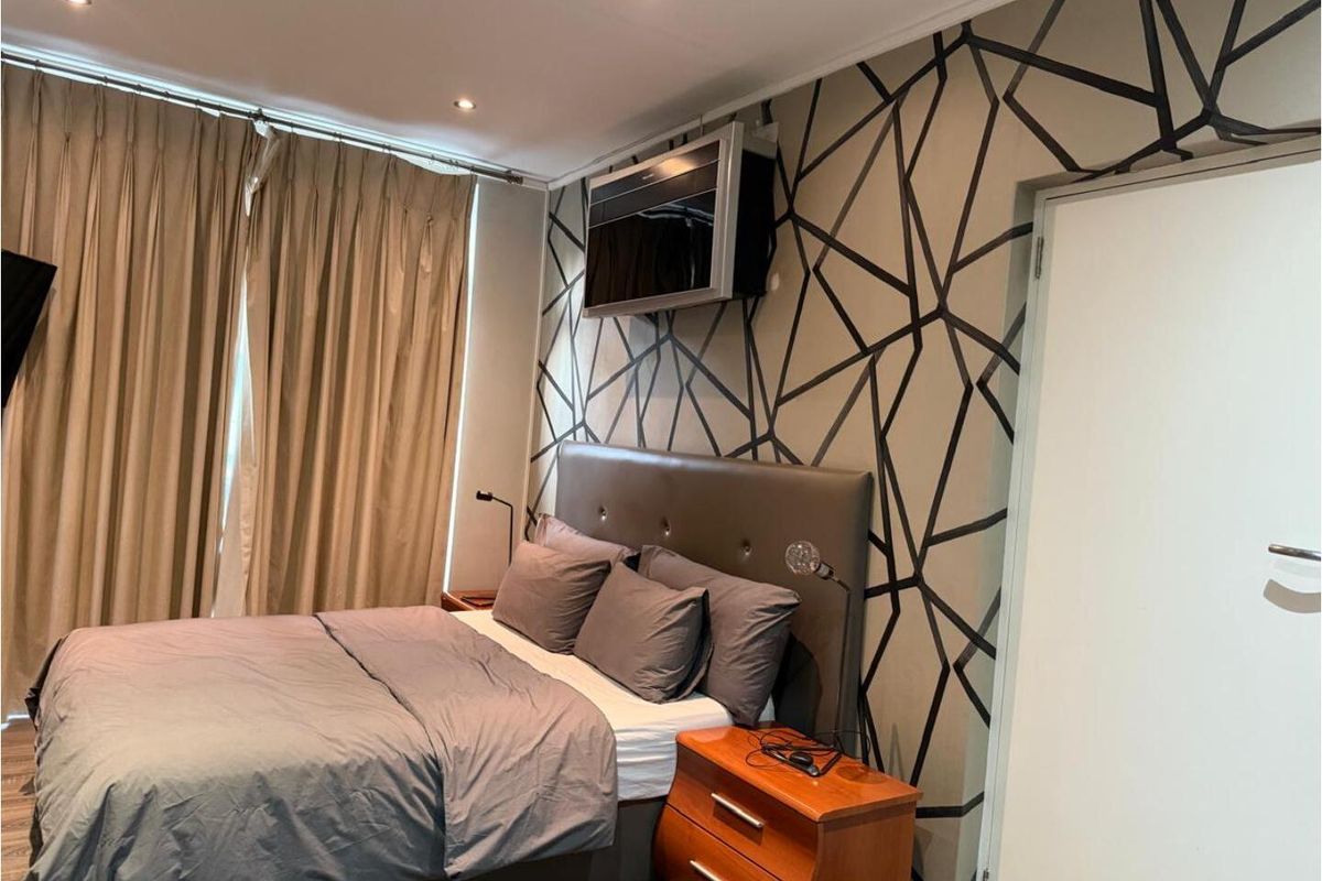 A well-maintained bedroom featuring recessed ceiling lighting, patterned feature wallpaper, and floor-to-ceiling curtains.