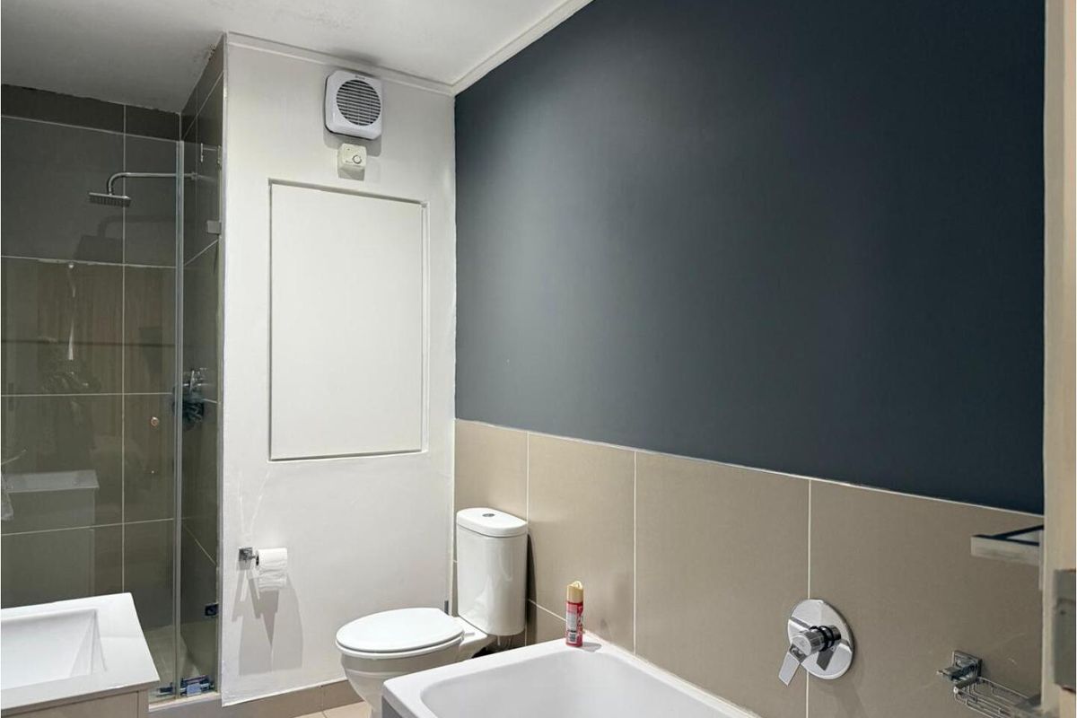 Modern bathroom featuring a glass-enclosed shower, a bathtub with chrome fixtures, a toilet, and a vanity basin with neutral wall tiling.