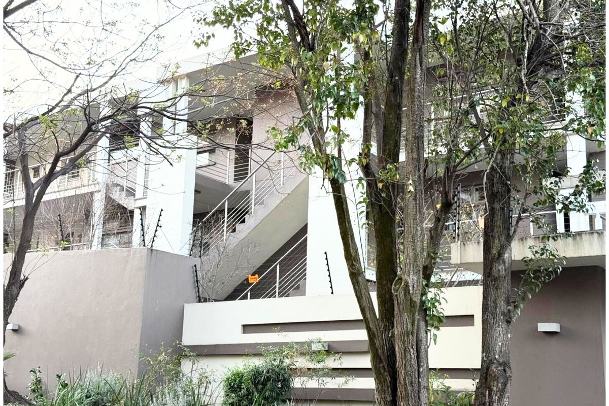 Exterior view of a modern apartment complex featuring multi-level balconies, external staircases with metal railings, and perimeter security fencing.