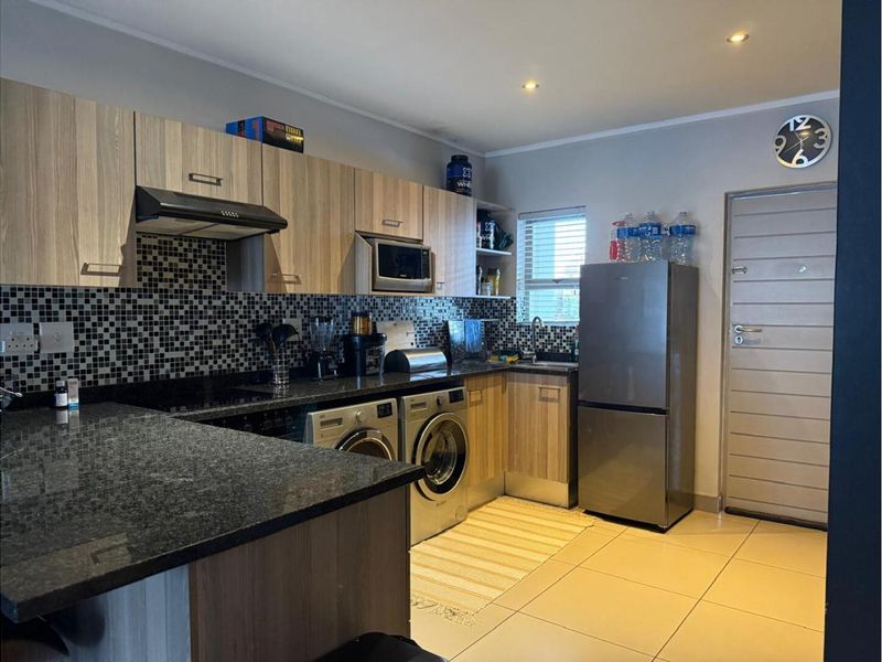 Modern kitchen featuring wood-grain cabinetry, granite countertops, mosaic tile backsplash, and integrated space for laundry appliances.