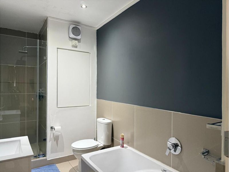 Modern bathroom featuring a glass-enclosed shower, a bathtub with chrome fixtures, a toilet, and a vanity basin with neutral wall tiling.