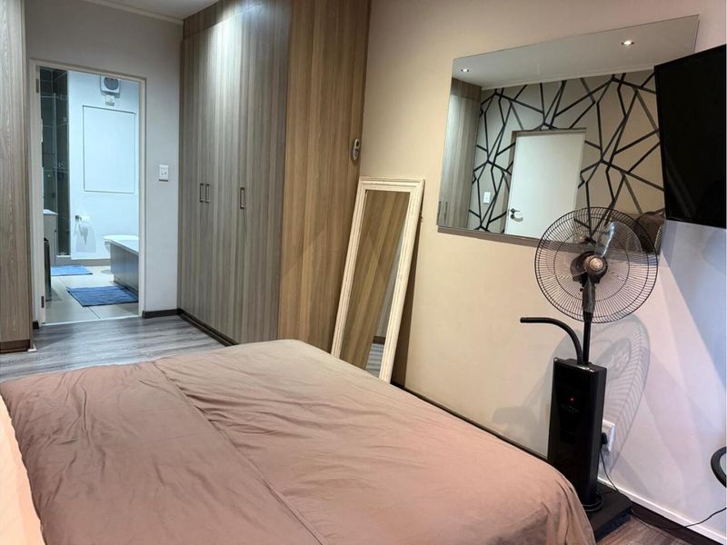 A well-maintained bedroom featuring built-in wooden cupboards, laminate flooring, and an en-suite bathroom with modern finishes.