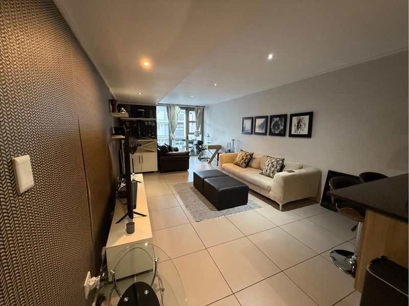 Open plan living area featuring large format floor tiles, recessed downlighting, and a textured feature wall leading to a balcony.