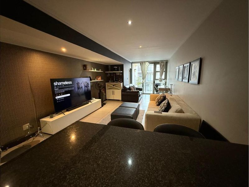 Open plan living area featuring tiled flooring, recessed lighting, and a built-in bar area, leading to a balcony with natural light.