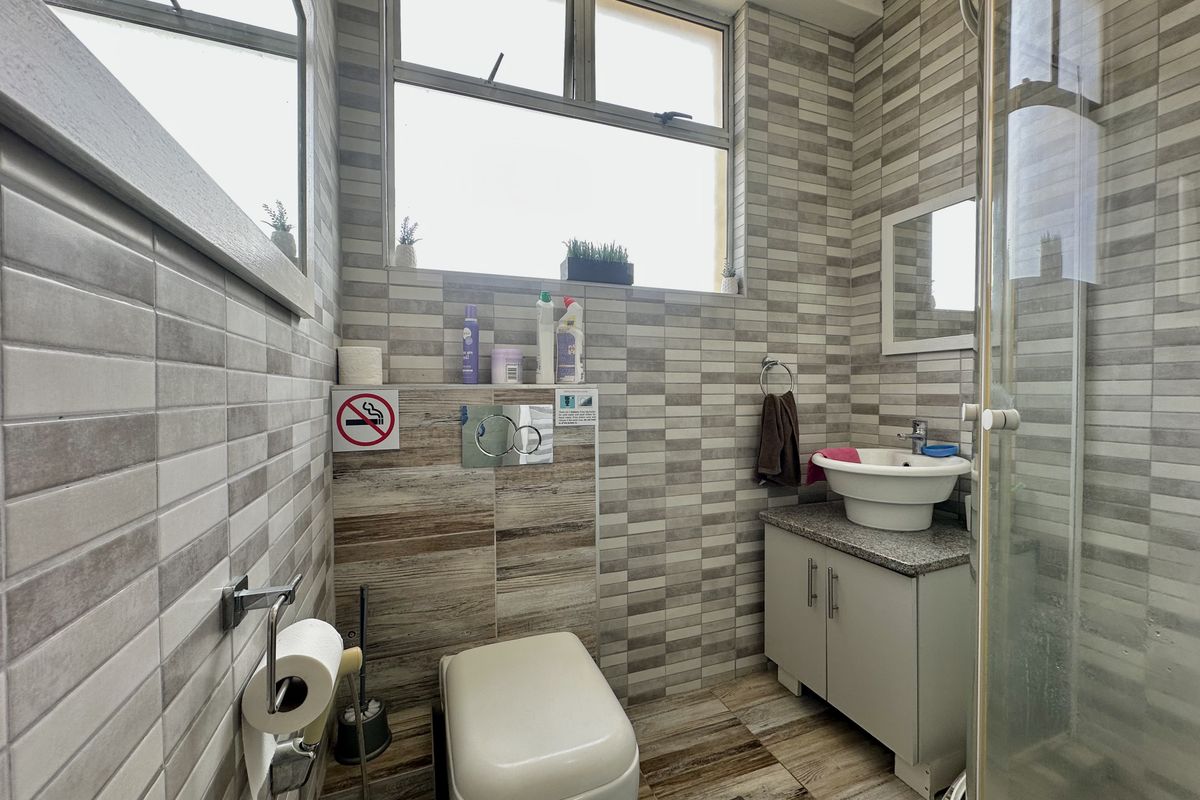 A compact bathroom featuring a wall-mounted toilet with a concealed cistern, a vessel sink on a vanity cabinet, and a glass shower enclosure.