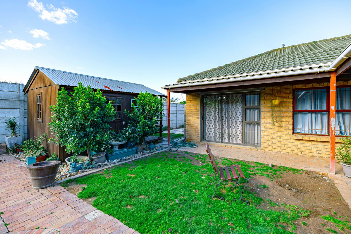 Rear garden area featuring a brick house with a paved patio, sliding doors, and a detached wooden storage shed.