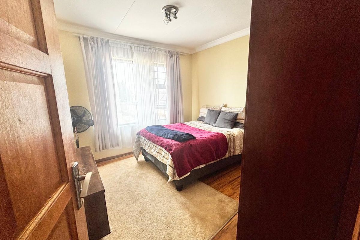 A standard bedroom featuring wooden flooring, a window with curtains, and a ceiling-mounted light fixture.