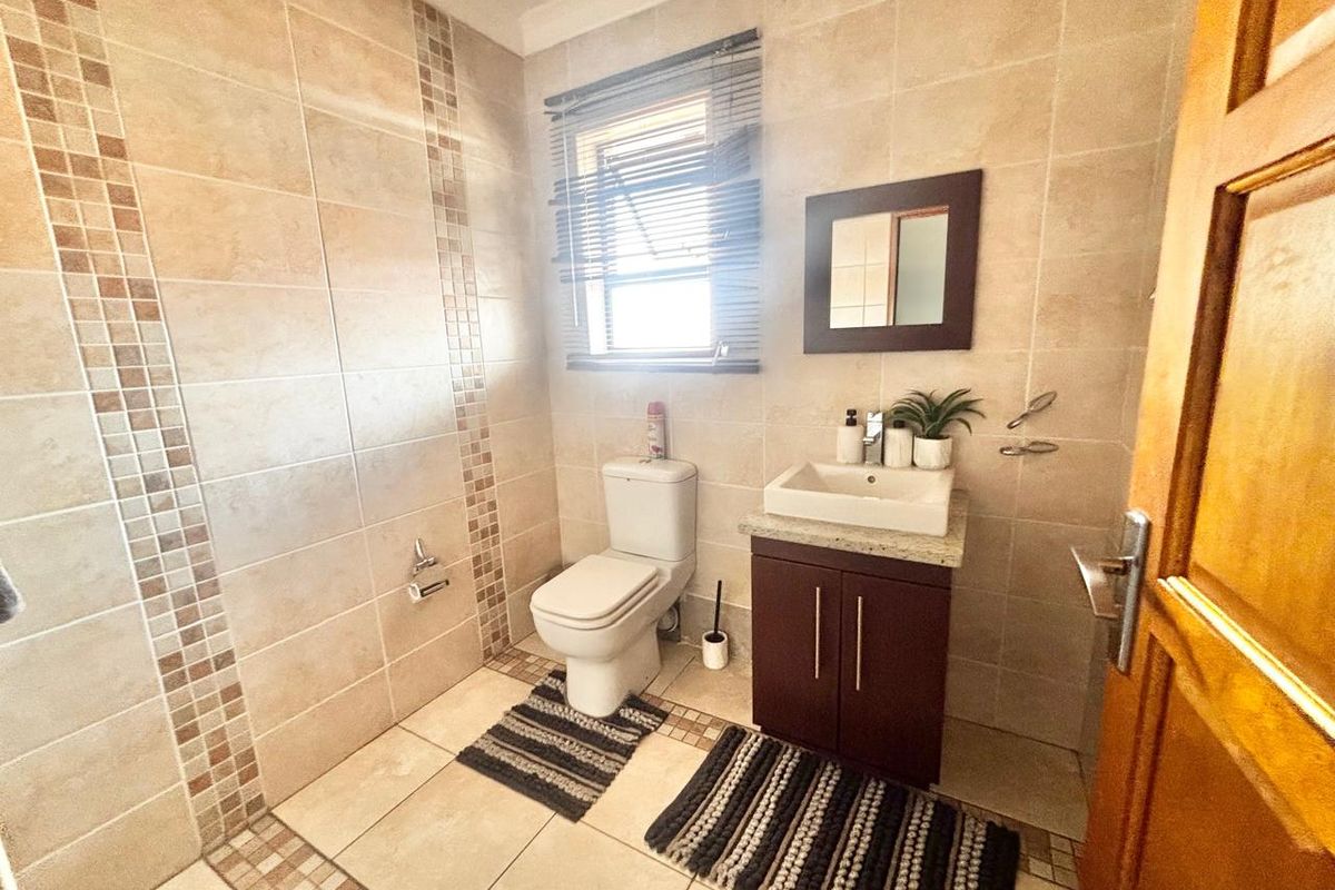 A functional bathroom featuring neutral wall tiles with decorative accents, a vanity unit with a basin, and a standard toilet.