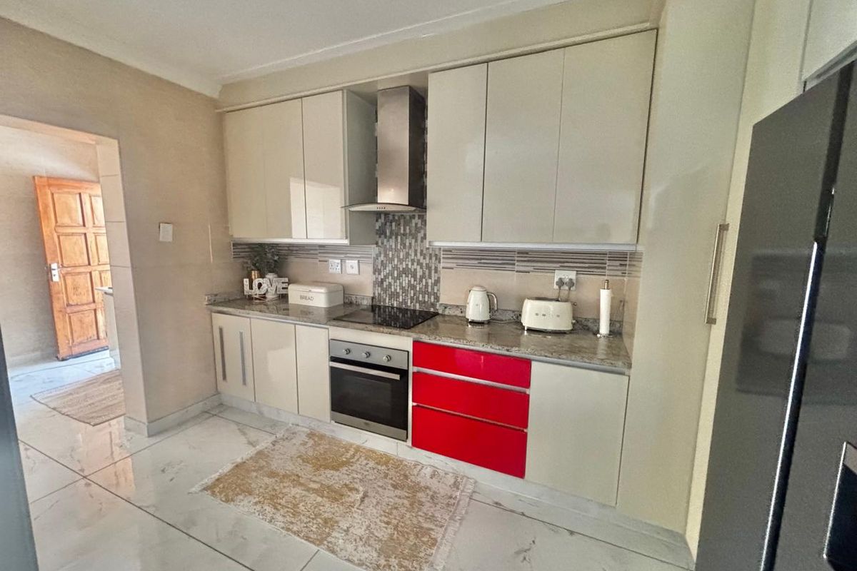 Modern kitchen featuring high-gloss cabinetry, granite countertops, built-in oven, glass hob, and stainless steel extractor fan with tiled flooring.