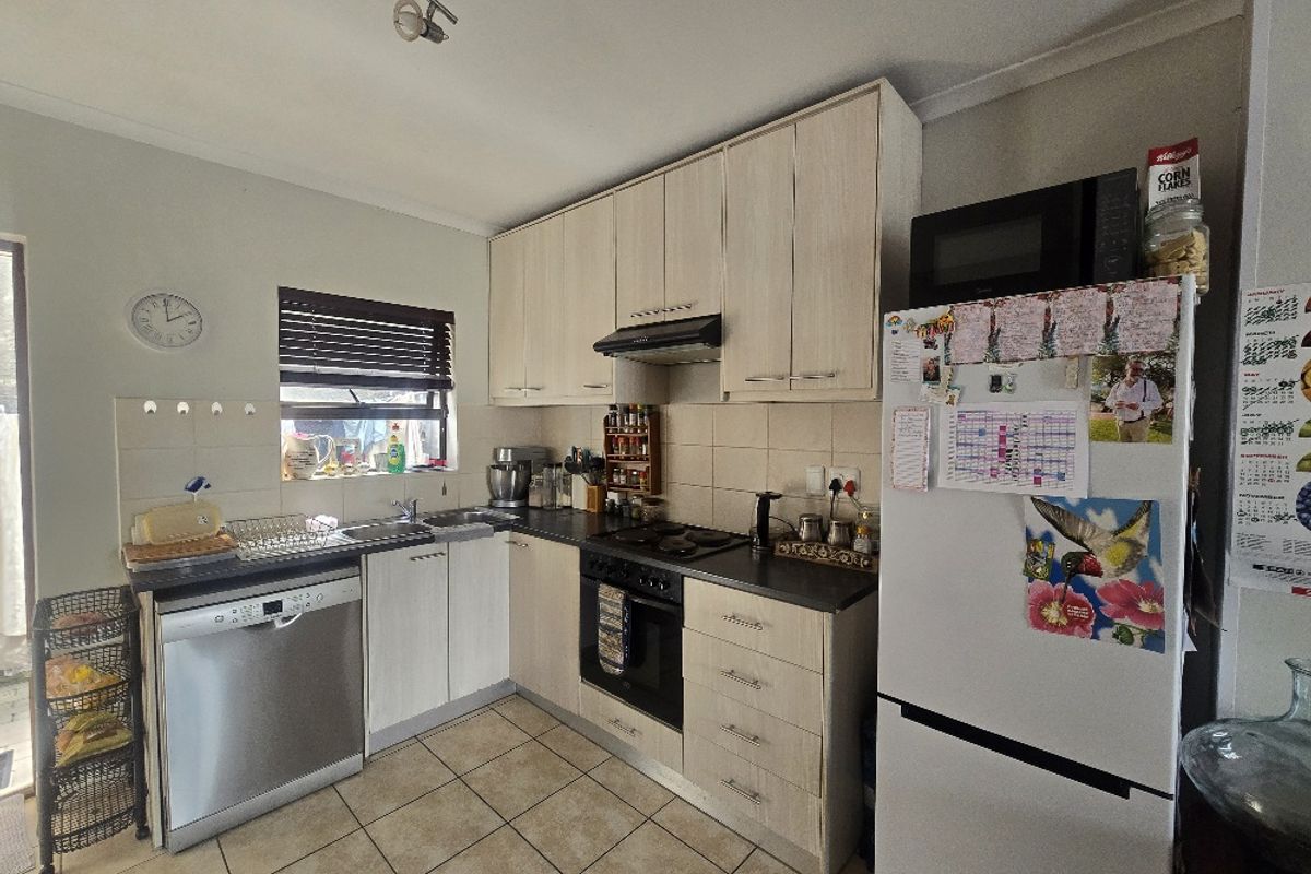 Functional kitchen featuring light wood-finish cabinetry, dark countertops, tiled flooring, and integrated cooking appliances including an oven, hob, and extractor fan.