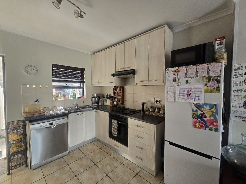 Functional kitchen featuring light wood-finish cabinetry, dark countertops, tiled flooring, and integrated cooking appliances including an oven, hob, and extractor fan.