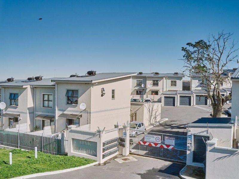 Aerial view of the Oak Woods townhouse complex entrance, featuring secure gated access, asphalt driveway, and multiple residential units with metal roofing.