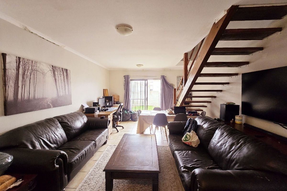 Open-plan living area featuring a wooden staircase, tiled flooring, and sliding door access to the rear exterior, showing signs of ceiling water damage.