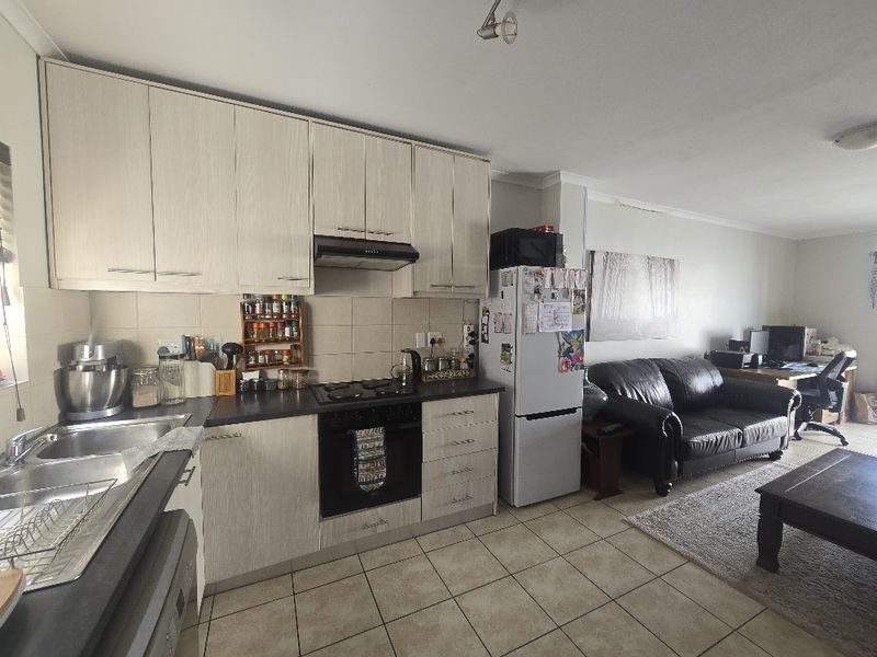 Open-plan kitchen and living area featuring light wood-finish cabinetry, built-in oven, gas hob, and tiled flooring throughout the space.
