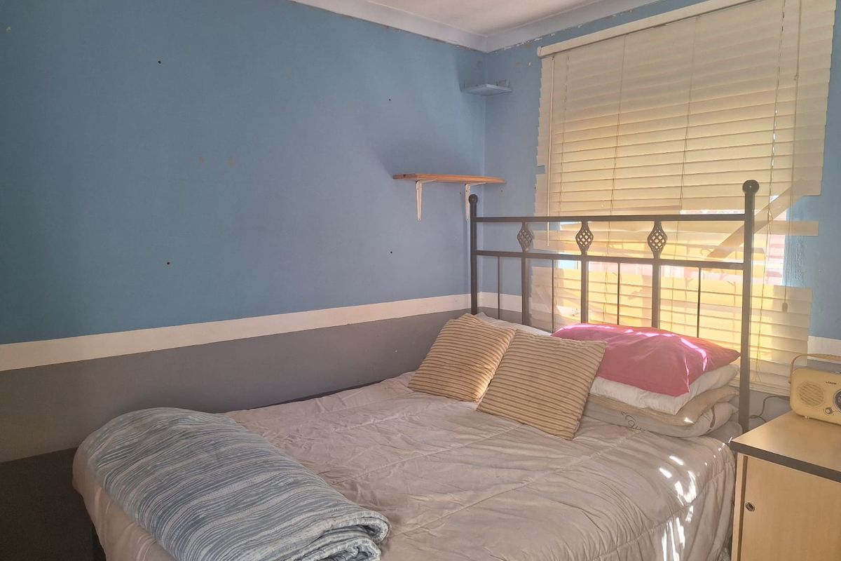 A bedroom featuring blue and grey painted walls, a window with fitted venetian blinds, and a wall-mounted shelf.