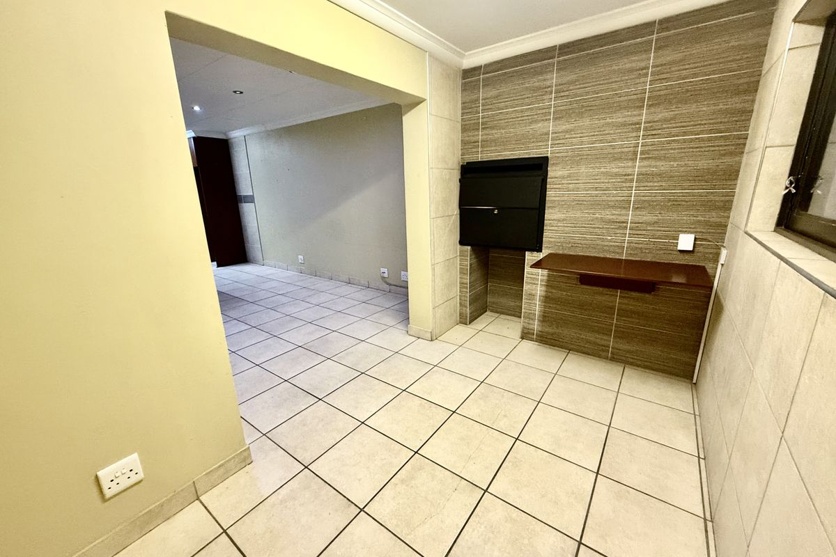 An interior view of a tiled living area featuring a built-in fireplace and a wooden shelf, leading into an adjacent room.
