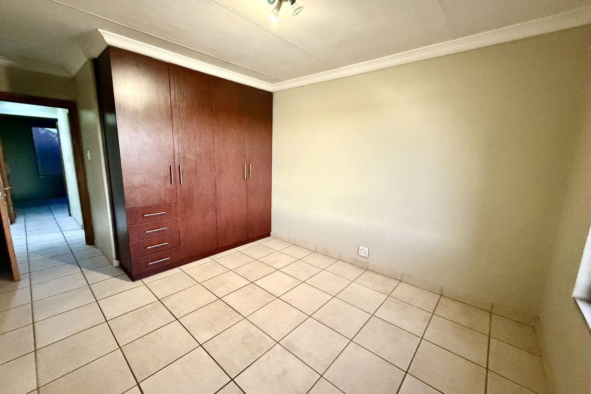 A bedroom featuring built-in wooden cupboards and tiled flooring, offering a functional and neutral space.