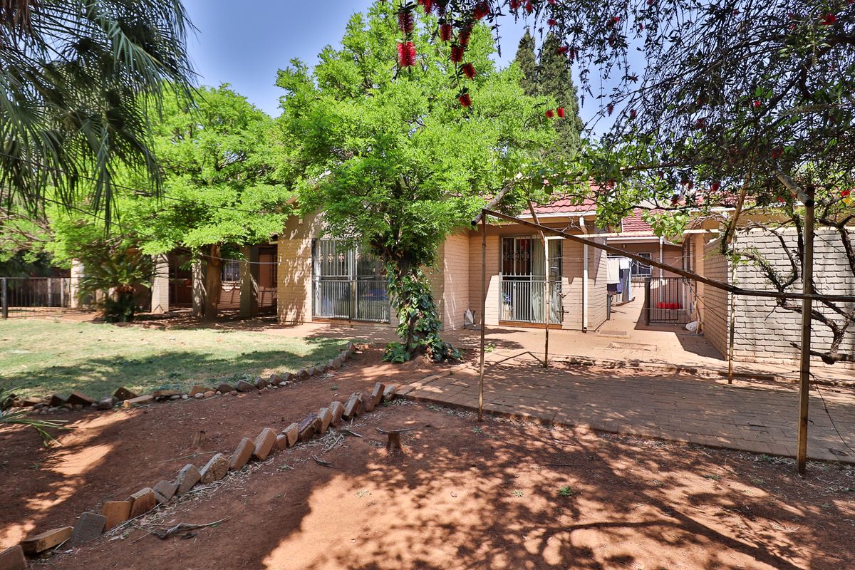 Rear view of the property featuring a brick facade, paved patio area, and established garden with mature trees.