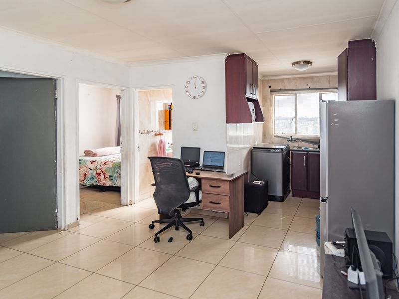 Open-plan living area featuring tiled flooring and a compact kitchen with built-in cabinetry, providing a functional layout for daily living.