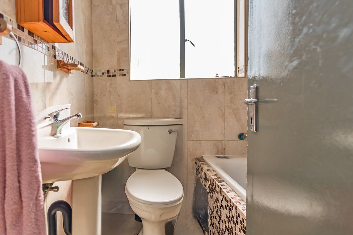 Compact bathroom featuring a pedestal basin, toilet, and bathtub with mosaic tile accents, requiring minor cosmetic updates to the tiling and finishes.