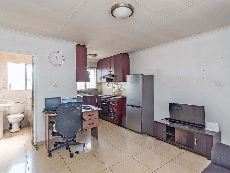 Open-plan living area featuring tiled flooring and a compact kitchen with built-in cabinetry, oven, and extractor fan, adjacent to a bathroom.