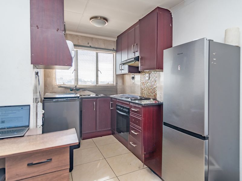 Compact kitchen featuring dark wood-look cabinetry, mosaic tile backsplash, built-in oven with hob, and tiled flooring.
