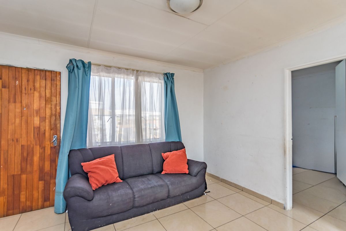 A living room featuring tiled flooring, a timber door, and a window with natural light, requiring cosmetic updates to improve its overall condition.