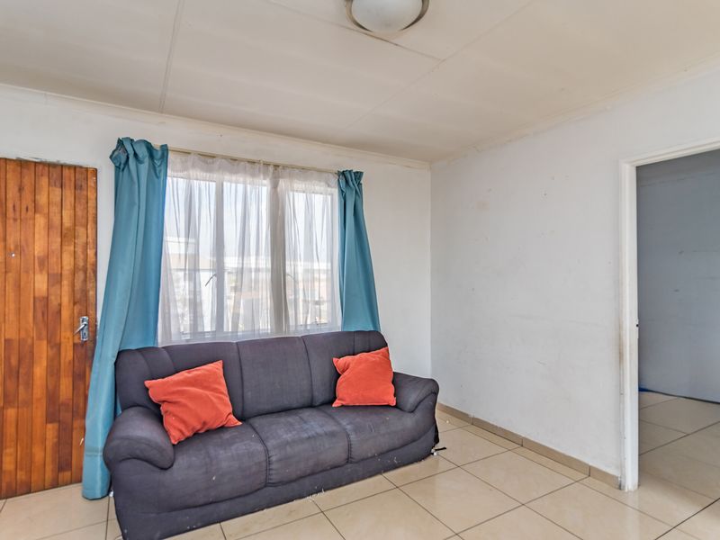 A living room featuring tiled flooring, a timber door, and a window with natural light, requiring cosmetic updates to improve its overall condition.