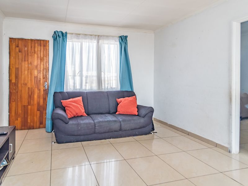 A living room featuring tiled flooring, a timber door, and a window, providing a functional space ready for cosmetic updates.