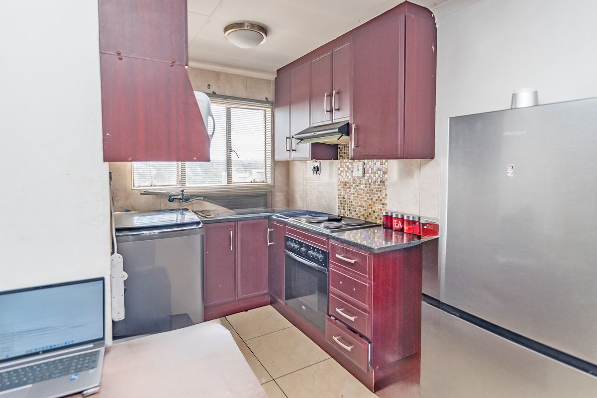 Compact kitchen featuring dark wood cabinetry, granite countertops, mosaic tile backsplash, and integrated oven and hob, providing a functional cooking space.