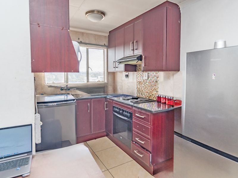 Compact kitchen featuring dark wood cabinetry, granite countertops, mosaic tile backsplash, and integrated oven and hob, providing a functional cooking space.