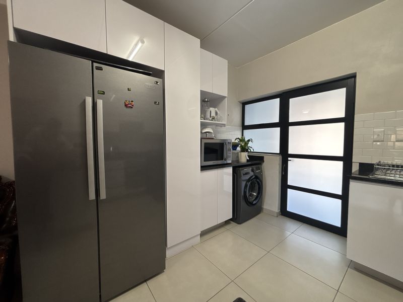A modern scullery featuring sleek white cabinetry, stone countertops, subway tile backsplash, and tiled flooring with direct access to an exterior door.