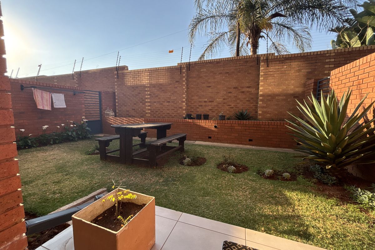 A private rear garden featuring a tiled patio area, a lawn, and a high brick boundary wall secured with electric fencing.