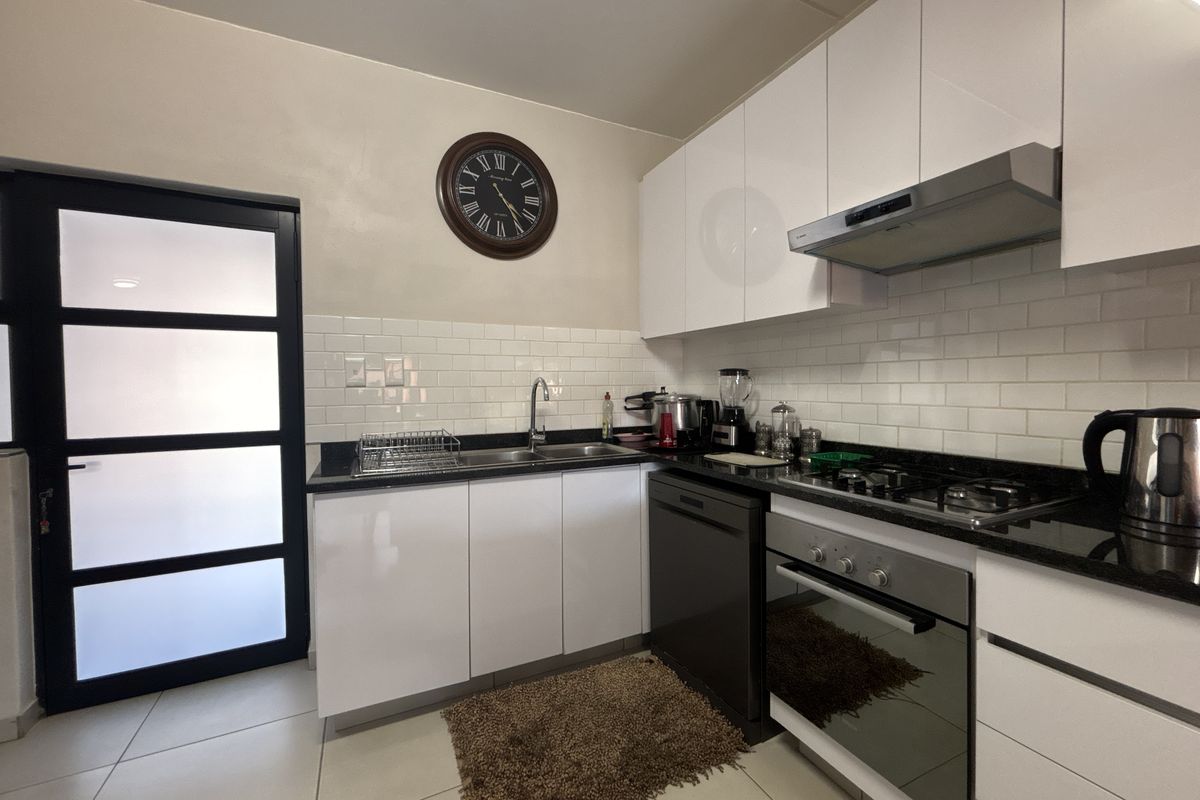 Modern kitchen featuring white gloss cabinetry, granite countertops, subway tile backsplash, and integrated stainless steel appliances including a gas hob and oven.