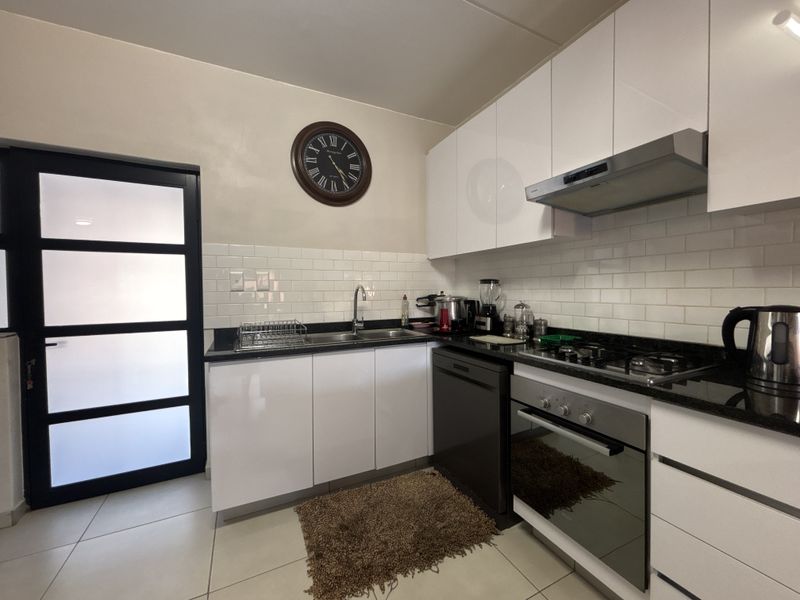 Modern kitchen featuring white gloss cabinetry, granite countertops, subway tile backsplash, and integrated stainless steel appliances including a gas hob and oven.