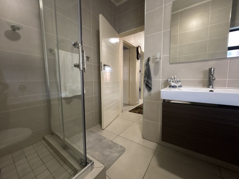 Modern bathroom featuring a glass shower enclosure, wall-mounted vanity with basin, and neutral ceramic tiling throughout.
