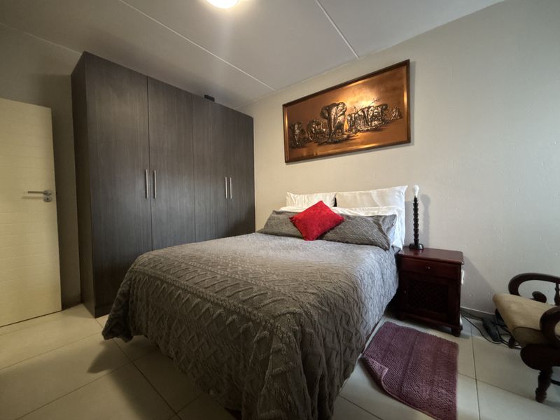 A well-maintained bedroom featuring neutral tiled flooring and a large, dark wood-finish built-in wardrobe providing ample storage space.
