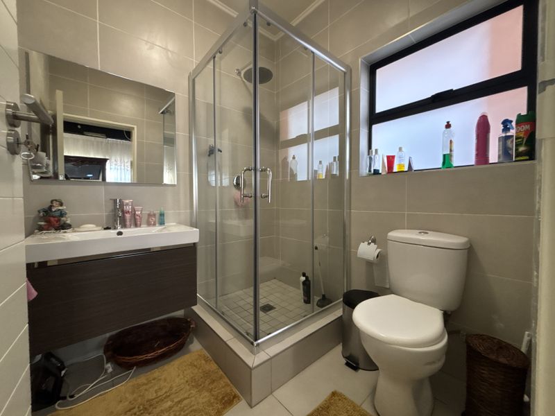Modern bathroom featuring a glass shower enclosure, wall-mounted vanity with basin, and tiled finishes throughout.
