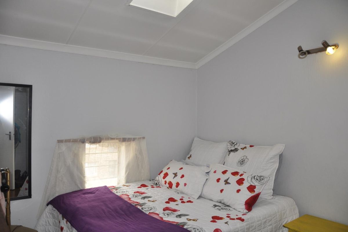 A bedroom featuring a skylight, wall-mounted spotlight, and a window with a curtain rod.