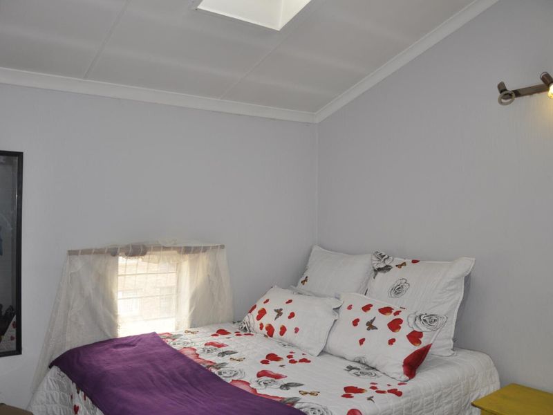 A bedroom featuring a skylight, wall-mounted spotlight, and a window with a curtain rod.