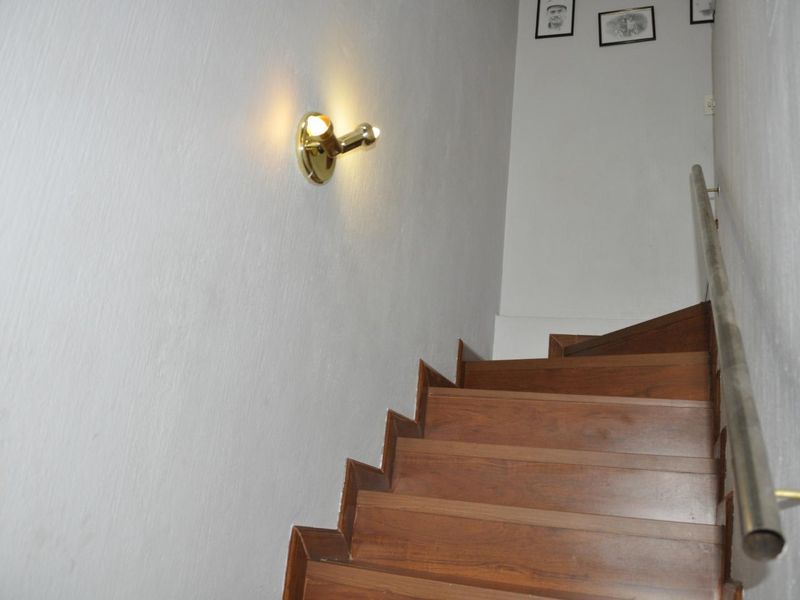 A staircase featuring wooden treads and a metal handrail, illuminated by a wall-mounted light fixture.