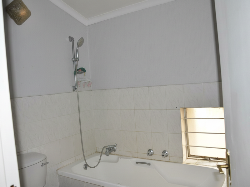 A functional bathroom featuring a built-in bathtub with a handheld shower attachment, tiled splashbacks, and a small window with security bars.