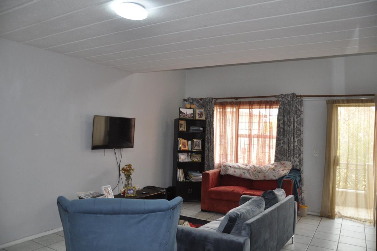A living room featuring tiled flooring, a ceiling with paneling, and a glass door providing access to an outdoor area.