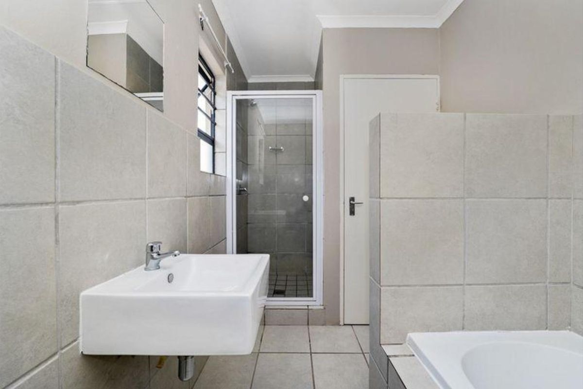 A functional bathroom featuring a wall-mounted basin, a separate glass-enclosed shower, and neutral floor-to-ceiling tiling.